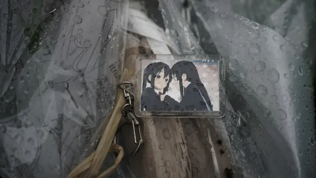 Seseorang menyelipkan gantungan kunci dengan gambar anime di atas karangan bunga yang diletakkan di Kyoto Animation (AP Photo/Jae C. Hong).