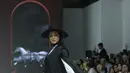 Ia terlihat elegan dalam pakaian monokrom, mengenakan dress panjang putih berkancing dengan aksen lengan puff. Dress tersebut dipadukan dengan outer panjang berkancing di bagian depan, yang memiliki desain cape pada lengan. Nabila juga mengenakan topi koboi hitam yang serasi dengan kerudung lilitnya.  [Dok/Fimela/Adrian Utama P].
