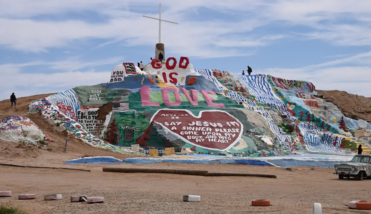 Turis mengunjungi Salvation Mountain, sebuah lereng bukti di Niland, California, Amerika Serikat. Dibangun dari kumpulan jerami, dempul jendela dan lebih dari 10,000 galon cat yang dipergunakan untuk membuat bukit tetap berdiri, dan melindunginya dari pasir dan angin gurun. (Robyn Beck/AFP)
