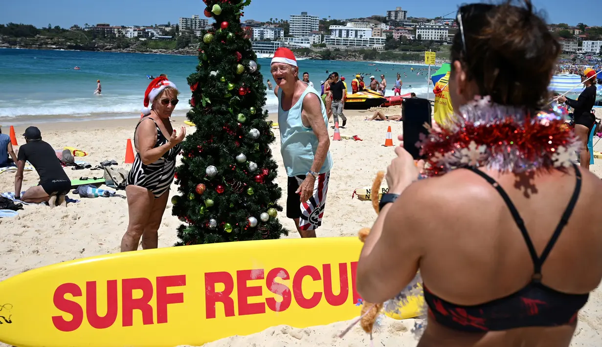 Seorang wanita mengenakan topi santa berjemur selama  Hari Natal 2018 di Pantai Bondi di Sydney, Australia (25/12). (AFP Photo/Peter Parks)