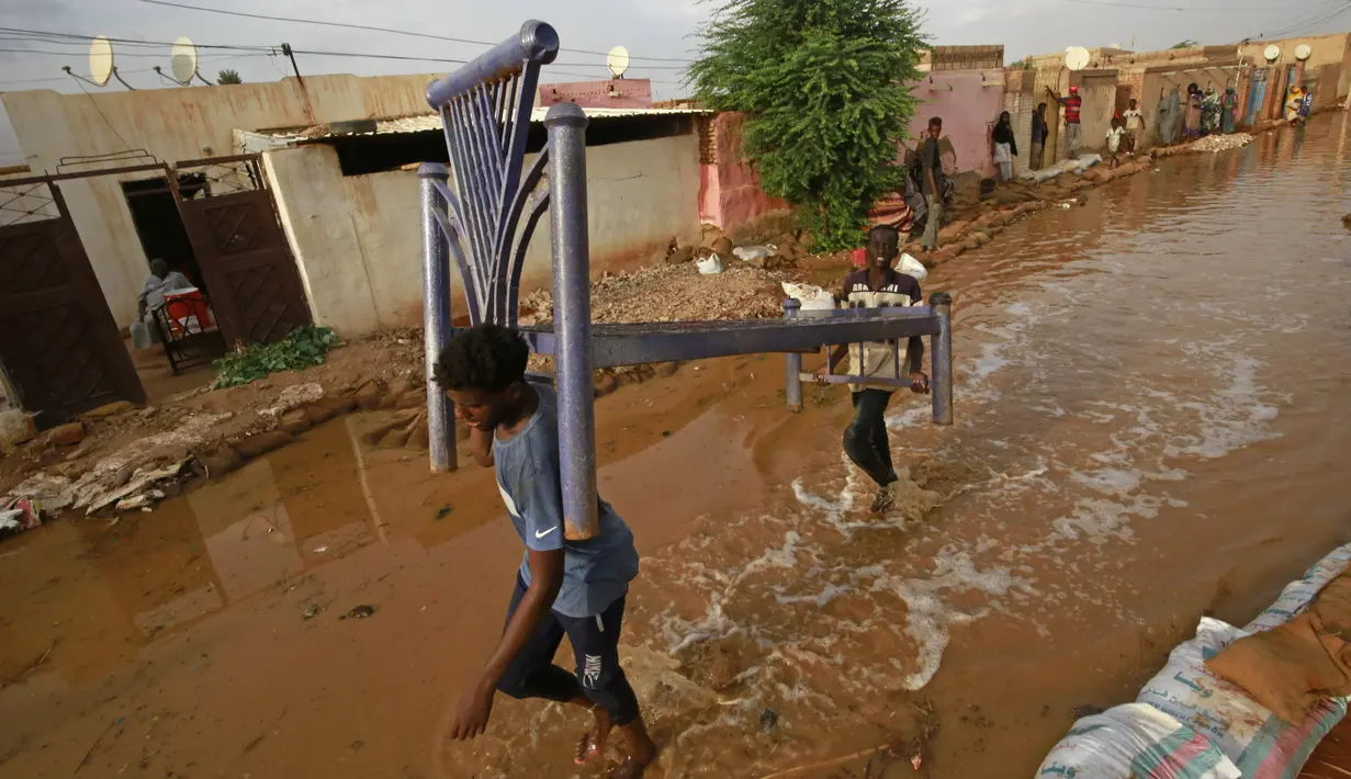 Pemuda Sudan membawa kerangka tempat tidur saat mereka melewati jalan banjir di daerah alqamayir di kota kembar ibu kota Omdurman (26/8/2020). (AFP Photo/Ashraf Shazly)