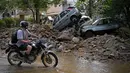 Seorang pria mengendarai sepeda motornya melewati mobil yang hancur akibat banjir bandang di Petropolis, Brasil, 16 Februari 2022. Banjir berskala besar menghancurkan ratusan properti dan menewaskan sebanyak 54 orang di daerah tersebut. (CARL DE SOUZA/AFP)