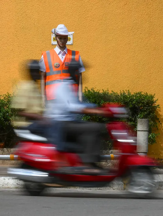 Pengendara melintasi manekin pria berseragam polisi lalu lintas di persimpangan jalan di Bangalore, India, Senin (16/12/2019). Polisi manekin itu diharapkan bisa mengelabui pengemudi yang akan mengiranya sebagai polisi asli sehingga mengurungkan niat melanggar lalu lintas. (Manjunath KIRAN / AFP)