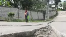 Seorang warga melintasi jalan yang terbelah akibat pergeseran tanah di kawasan Bojong Koneng, Babakan Madang, Kabupaten Bogor, Jawa Barat, Jumat (16/9/2022). Badan Penanggulangan Bencana Daerah (BPBD) setempat mencatat 18 unit rumah mengalami kerusakan, dan pergeseran tanah itu menyebabkan retakan-retakan di tanah, dinding, plafon dan lantai rumah warga serta akses jalan sudah tidak bisa dilewati oleh kendaraan roda dua dan roda empat. (Liputan6.com/Herman Zakharia)