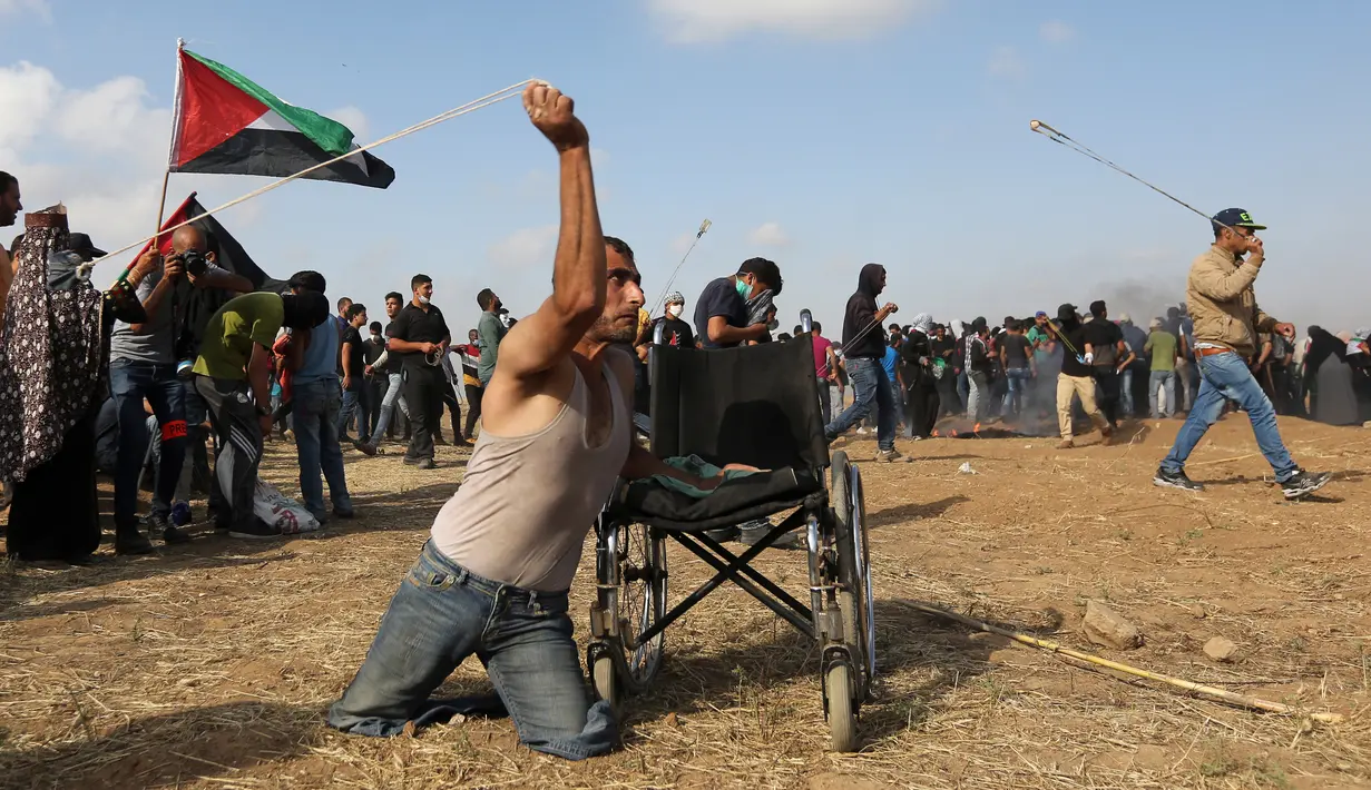 Seorang pria Palestina bernama Saber al-Ashkar melemparkan batu bersanggakan kursi rodanya saat terlibat bentrok dengan pasukan Israel di dekat perbatasan antara Israel dengan Jalur Gaza (11/5). (AFP/Mahmud Hams)
