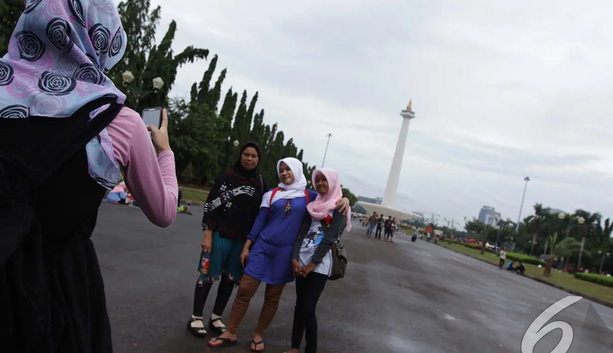 Para pengunjung mengabadikan gambar mereka dengan latar pemandangan tugu Monas, Jakarta, Kamis (1/1/2015). (Liputan6.com/Faizal Fanani)