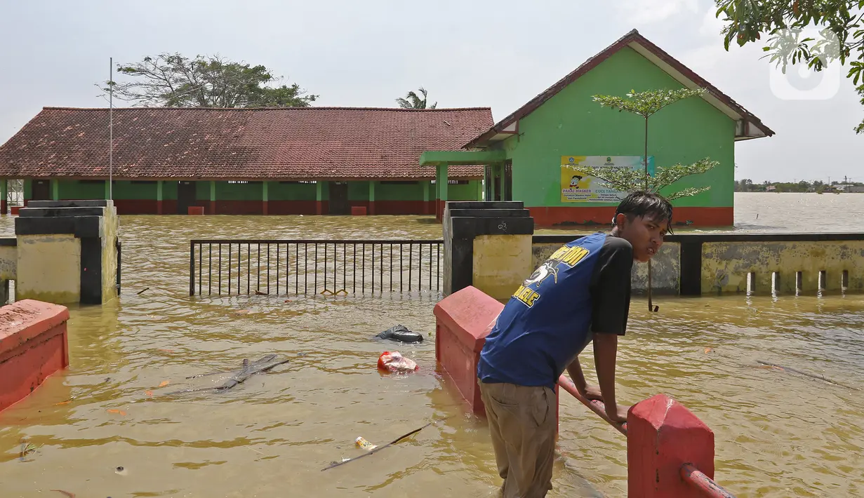 Seorang anak berada di depan sekolah yang terendam banjir di Desa Sukalaksana Kabupaten Bekasi, Jawa Barat, Senin (22/02/2021). Banjir tersebut akibat luapan sungai Citarum yang tanggulnya jebol. (Liputan6.com/Herman Zakharia)