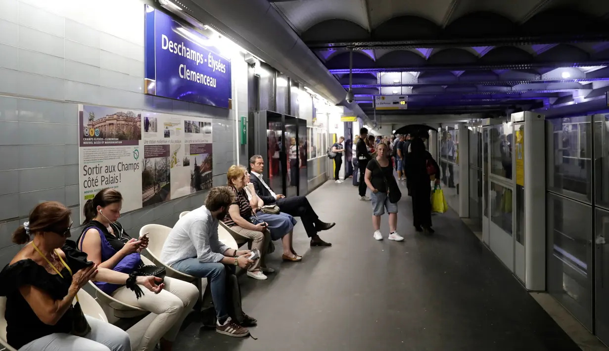 Para komuter duduk dekat tanda yang bertuliskan "Deschamps - Elysees Clemenceau" di stasiun metro Champs - Elysees Clemenceau, Paris, Senin (16/7). Hal itu untuk merayakan kesuksesan timnas Prancis menjadi juara Piala Dunia. (AFP/Thomas SAMSON)