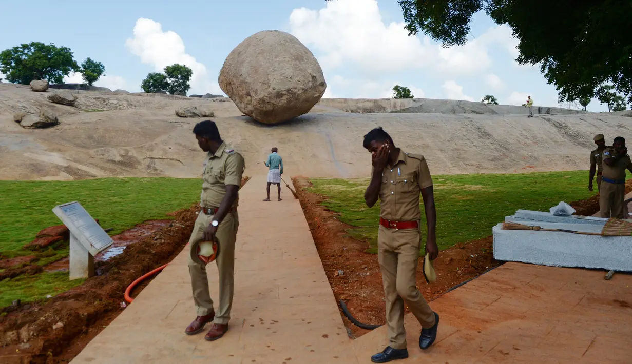 Polisi India berjalan melewati batu 'Krishna's Butter Ball' yang terkenal di Mahabalipuram, Kamis (3/10/2019). Selama 1.300 tahun, batu raksasa seberat 250 ton ini tampak seperti melawan gravitasi. (ARUN SANKAR / AFP)