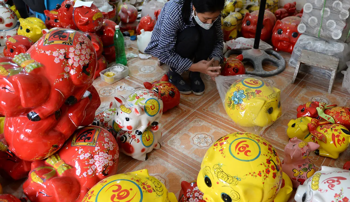 Perajin membungkus patung-patung babi tanah liat yang berwarni-warni menjelang Tahun Baru Imlek atau Tet di sebuah bengkel, Hanoi, 23 Januari 2019. Vietnam bersiap merayakan Tahun Baru Imlek 2019 yang merupakan tahun shio babi tanah. (Nhac NGUYEN/AFP)