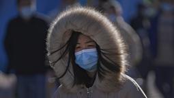 Seorang wanita mengenakan masker untuk membantu mengekang penyebaran virus corona bersiap menghadapi angin dingin saat dia berjalan di dekat distrik perbelanjaan Wangfujing di Beijing, Minggu (12/12/2021). (AP Photo/Andy Wong)