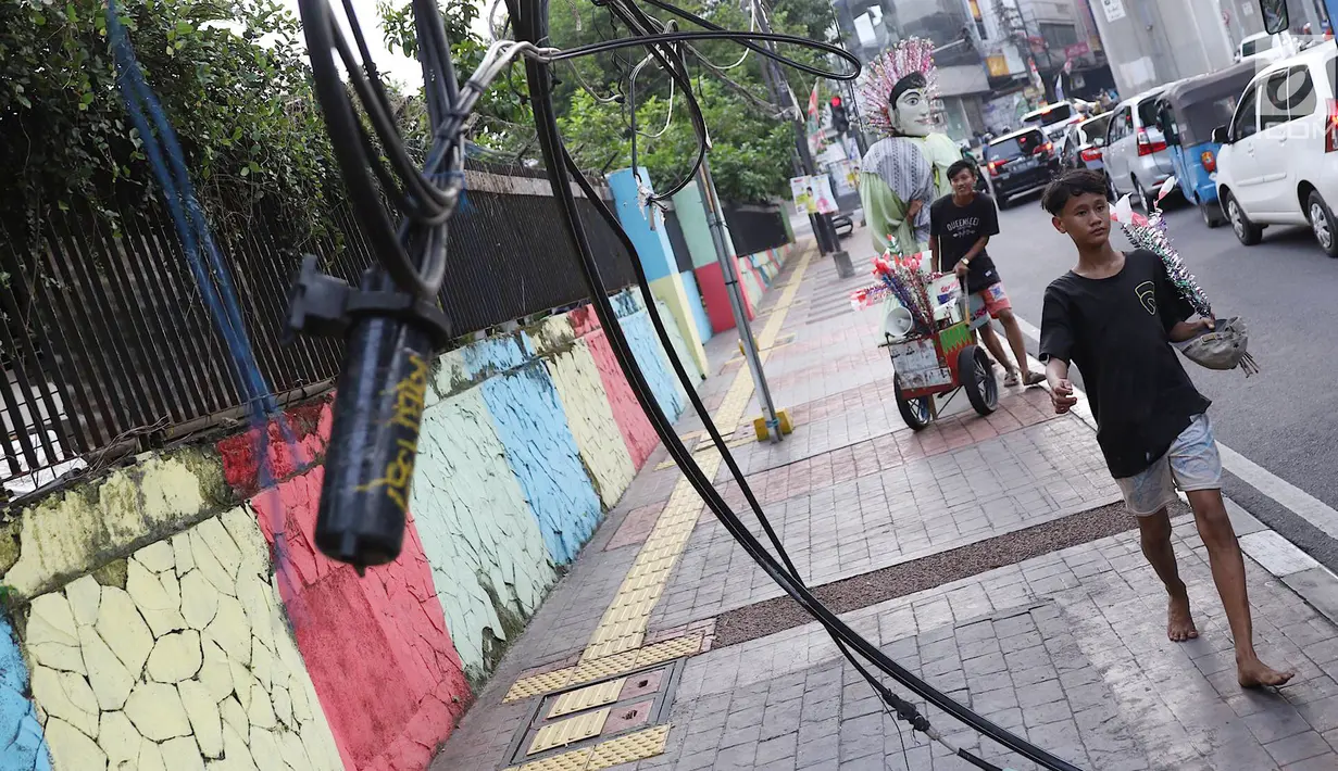 Pejalan kaki melintasi trotoar yang terhalang instalasi kabel di Jalan Kyai Maja, Jakarta, Rabu (10/4). Selain menganggu kenyamanan pejalan kaki, kondisi instalasi kabel yang semrawut tersebut juga berbahaya apabila mengandung aliran listrik. (Liputan6.com/Immanuel Antonius)