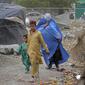 Seorang perempuan yang mengenakan burqa dan anak-anaknya berjalan di depan rumah mereka di Kabul, Afghanistan, 8 Mei 2022. Taliban memerintahkan perempuan Afghanistan untuk mengenakan pakaian dari kepala hingga ujung kaki atau burqa tradisional di depan umum. (AP Photo/Ebrahim Noroozi)