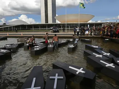 Sejumlah orang menceburkan replika peti mati saat menggelar aksi protes di luar gedung Kongres Nasional di Brasilia, Brasil (25/4). Mereka menuntut pertanggung jawaban atas terbunuhnya orang Indian karena masalah demarkasi lahan. (AP Photo/Eraldo Peres)