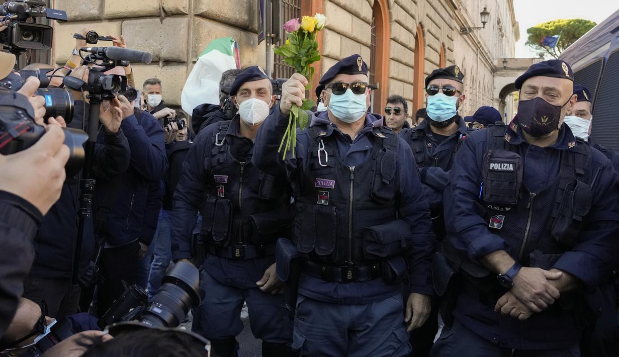 Petugas polisi memegang bunga yang diberikan demonstran selama aksi protes di Circus Maximus Roma, Jumat (15/10/2021). Protes tersebut karena aturan yang mengharuskan seluruh pekerja di Italia menunjukkan kartu kesehatan covid-19 untuk memasuki tempat kerja mereka. (AP Photo/Gregorio Borgia)
