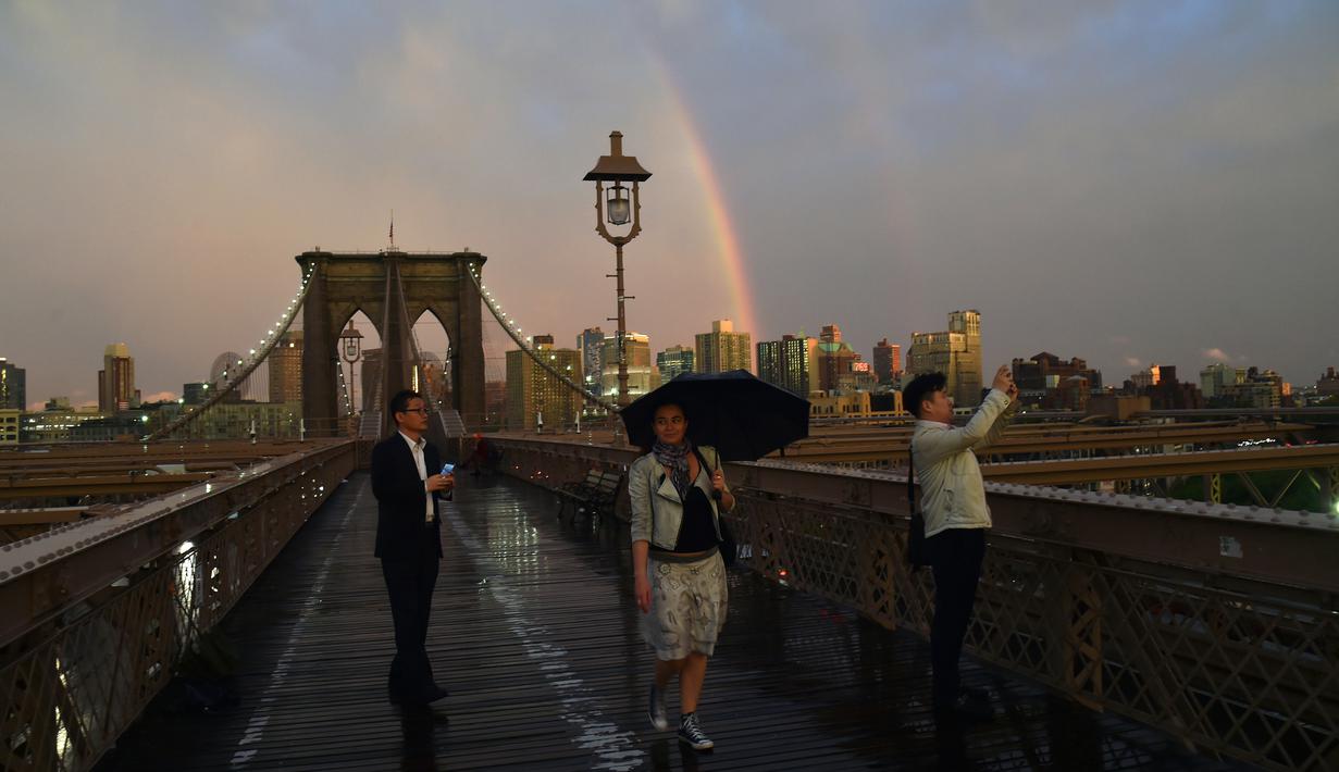 Warga mengabadikan keindahan pelangi dari Jembatan Brooklyn di New York City, AS (15/5). Jembatan Brooklyn adalah salah satu jembatan suspensi tertua di Amerika Serikat. (AFP Photo/Hector Retamal)