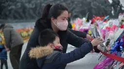 Seorang wanita dan seorang anak meletakkan karangan bunga saat memberi hormat di depan patung mendiang pemimpin Korea Utara Kim Il-sung dan Kim Jong-il pada peringatan 10 tahun kematian Kim Jong-il, Pyongyang, Korea Utara, 16 Desember 2021. Kim Jong-il adalah ayah dari Kim Jong-un. (KIM WON JIN/AFP)