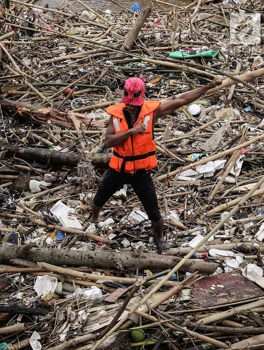 Petugas kebersihan berpose menggunakan topeng Spiderman membersihkan sampah yang menumpuk di Pintu Air Manggarai, Jakarta, Senin (12/11). (Liputan6.com/Fery Pradolo)