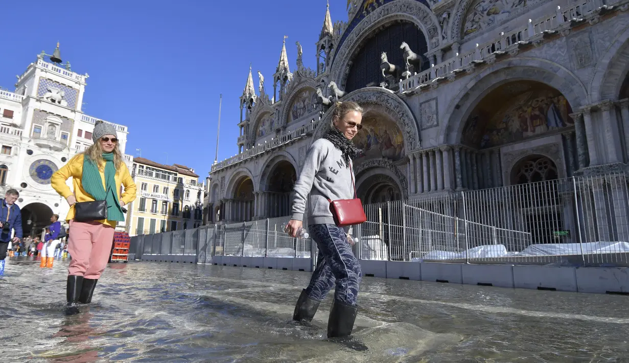 Orang-orang berjalan di St. Mark's Square yang terendam banjir di Venesia, Italia, Jumat (5/11/2021). Setelah Venesia mengalami banjir terparah kedua dalam sejarahnya pada November 2019, kota itu dibanjiri empat kali pasang luar biasa dalam waktu enam minggu. (AP Photo/Luigi Costantini)