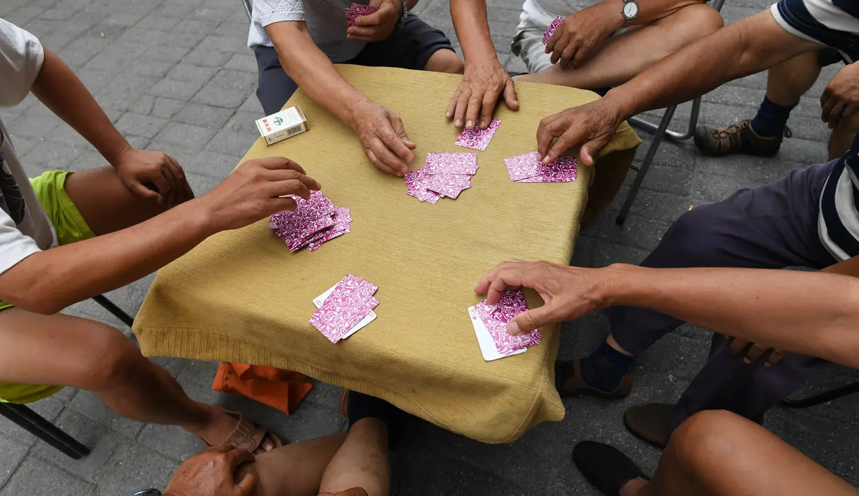 Sekelompok pria bersiap bermain kartu remi di trotoar di luar gedung apartemen di Beijing, China (10/8). Seperti kita kenal sekarang, satu pak kartu remi berisi 52 lembar. (AFP Photo/Greg Baker)