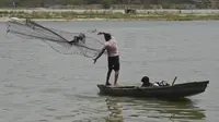 Nelayan melemparkan jala dari perahunya ke Sungai Yamuna di tengah meningkatnya suhu di New Delhi, Rabu (27/5/2020). Menurut Departemen Meteorologi India, gelombang panas diproyeksikan terjadi hingga beberapa hari ke depan. (Money SHARMA/AFP)