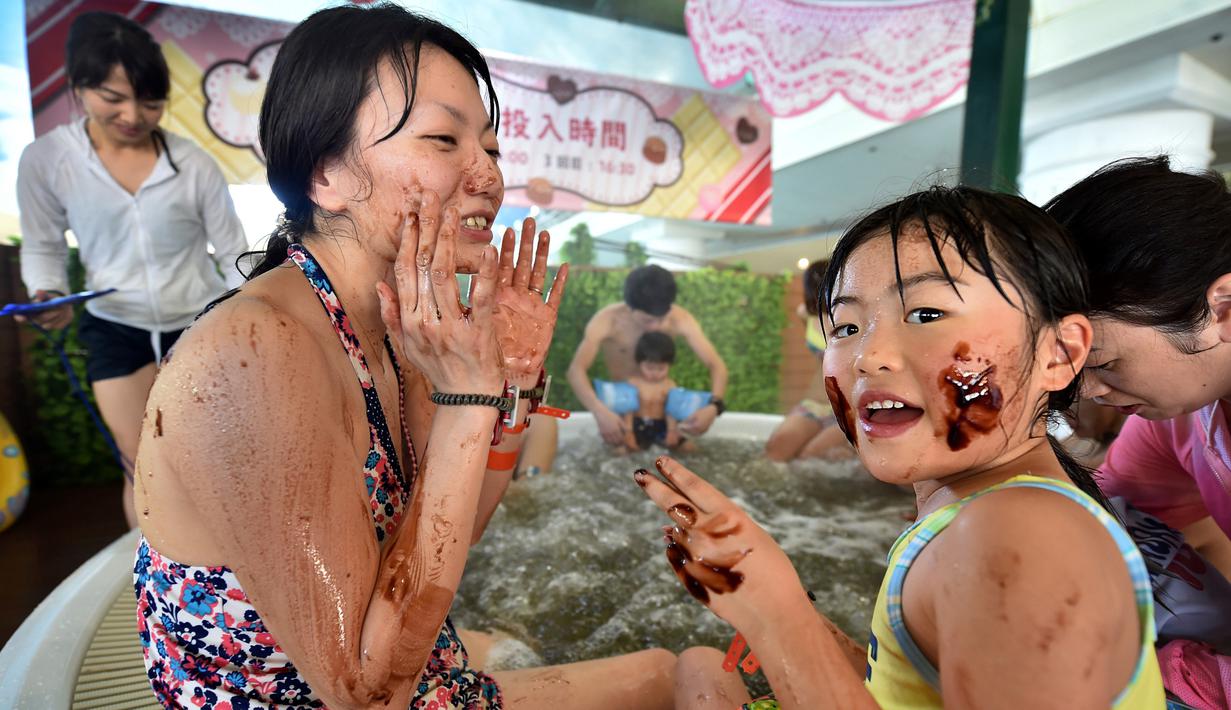 Seorang wanita dan putrinya menempelkan cokelat ke wajah mereka saat mandi spa cokelat di Hakone, Jepang, Senin (13/2). Mandi spa cokelat diadakan dalam rangka menyambut Hari Valentine. (AFP PHOTO / Kazuhiro Nogi)