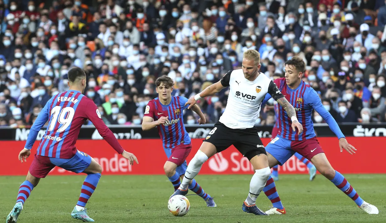 Gelandang Valencia, Uros Racic mengontrol bola dari kawalan para pemain Barcelona pada pertandingan La Liga Spanyol di stadion Mestalla, Spanyol, Minggu (20/2/2022). Barcelona menang atas Valencia 4-2. (AP Photo/Alberto Saiz)