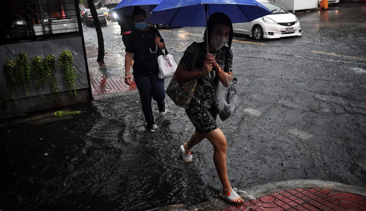 Orang-orang berjalan di jalan yang banjir saat hujan deras di Bangkok (23/9/2020). (AFP/Mladen Antonov)