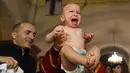 Seorang bayi menangis saat pendeta mengangkatnya dari air dalam acara pembaptisan massal di Gereja Katedral Holy Trinity, Tbilisi, Georgia (21/1). (AFP Photo/Vano Shlamov)
