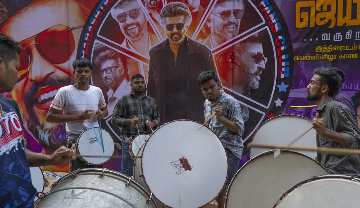 Para pemain drum bermain di dekat poster superstar India Rajinikanth, di luar gedung bioskop saat para penggemar merayakan pemutaran film terbarunya "Jailer" di Mumbai, India, Kamis (10/8/2023). (AP Photo/Rafiq Maqbool)