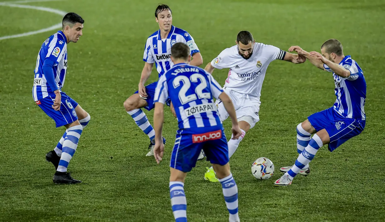 Penyerang Real Madrid, Karim Benzema berusaha melewati para pemain Deportivo Alaves pada pertandingan lanjutan La Liga Spanyol di stadion Mendizorroza di Vitoria. Minggu (24/1/2021). Benzema menjadi bintang kemenangan Los Blancos dengan torehan dua golnya. (AP Photo/ Alvaro Barrientos)