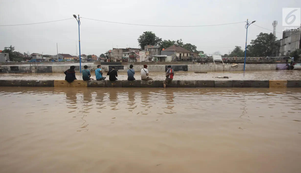 Sejumlah warga duduk di pembatas jalan saat banjir menggenangi Jalan Jatinegara Barat, Jakarta Timur, Selasa (6/2). (Liputan6.com/Arya Manggala)