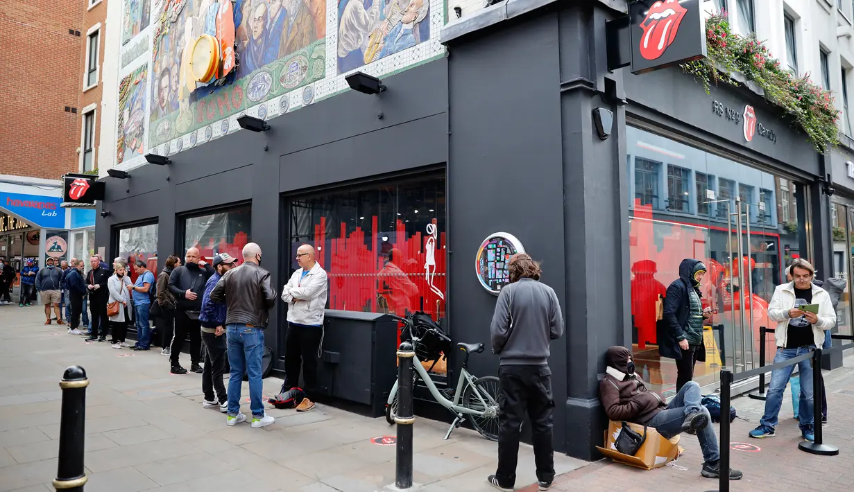 Orang-orang mengantre untuk memasuki toko andalan The Rolling Stones yang baru sebelum hari pertama pembukaannya di London, Rabu (9/9/2020). Toko tersebut akan menjual busana dan merchandise, serta musik, dari band rock The Rolling Stones. (Tolga Akmen / AFP)