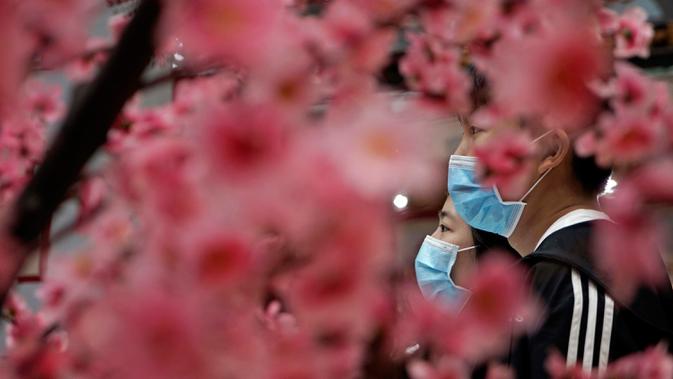 Orang-orang yang mengenakan masker berjalan melewati dekorasi perayaan Imlek Tahun Tikus Logam di Hong Kong, 24 Januari 2020. Pemerintah China memutuskan menutup seluruh akses masuk dan keluar Kota Wuhan untuk mencegah penyebaran wabah virus corona. (AP/Kin Cheung)