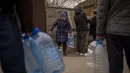 Penduduk setempat mengisi botol mereka dengan air yang mereka ambil dari air mancur umum di Bucha, di pinggiran Kiev, Ukraina pada Senin (18/4/2022). Warga Bucha masih tanpa listrik, air dan gas setelah lebih dari 43 hari sejak invasi Rusia. (AP Photo/Emilio Morenatti)