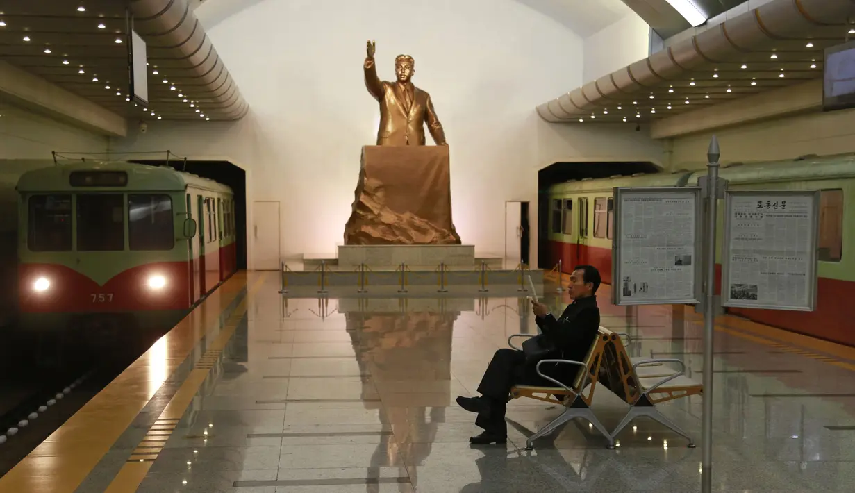 Seorang pria membaca sambil menunggu kereta dengan latar belakang patung mendiang Presiden Korea Utara Kim Il Sung di stasiun kereta bawah tanah Kaeson di Pyongyang, Korea Utara (23/11/2019). Stasiun Kaeson adalah stasiun di Jalur Chŏllima Metro Pyongyang. (AP Photo/Dita Alangkara)