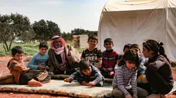 Abderrazaq Khatoun, beristirahat dengan 11 cucunya yang yatim piatu di luar tenda di desa Harbanoush, di Idlib, Suriah pada 11 Maret 2021. Perang Suriah yang merampas 13 anak Khatoun dan salah satu istrinya, membuat kakek 83 tahun itu membesarkan 11 cucu yatim piatu sendirian. (Ahmad al-ATRASH/AFP)