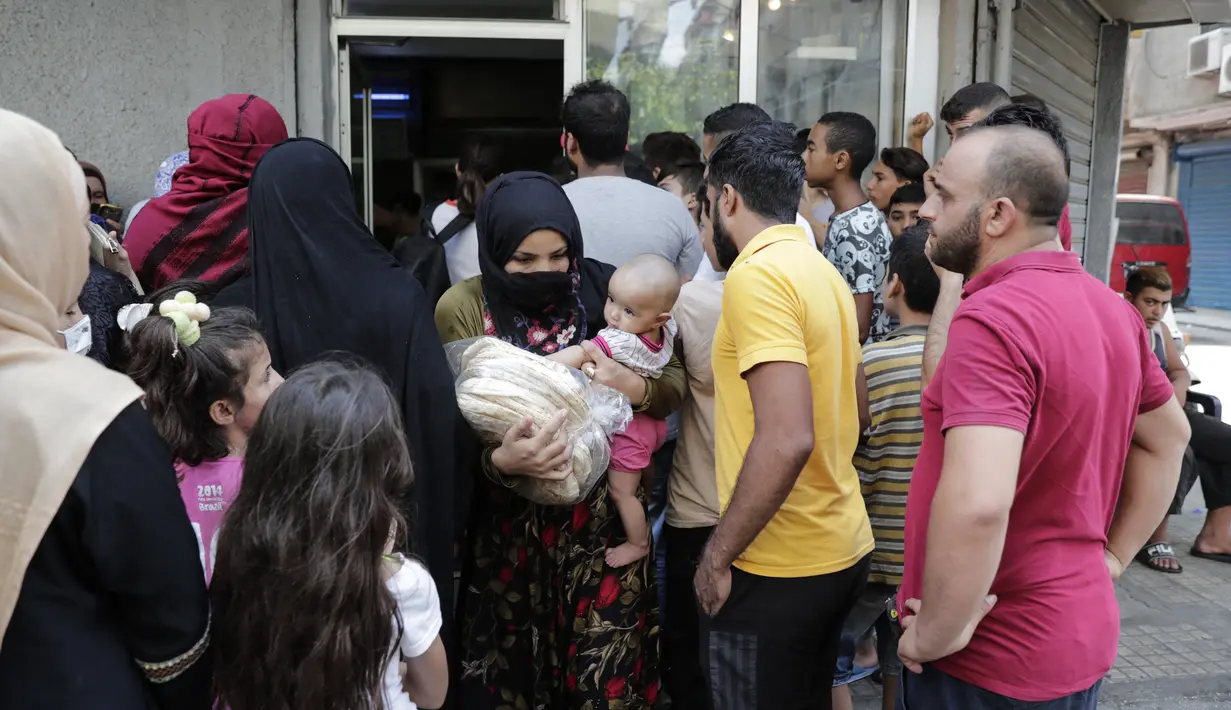 Seorang wanita membawa balita meninggalkan toko roti saat orang-orang menunggu giliran, di lingkungan Nabaa, Beirut, (13/8/2021). Tanpa masker, warga Lebanon berbondong-bondong ke toko roti untuk membeli roti yang terjangkau ketika pasokan bahan bakar dan obat-obatan terbatas. (ANWAR AMRO/AFP)