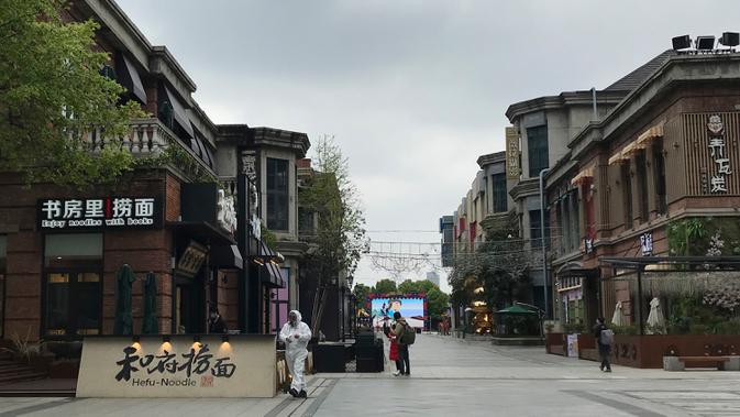 Penjaga toko mengenakan pakaian pelindung menunggu pelanggan di sebuah jalan ritel di Wuhan di provinsi Hubei, China tengah (30/3/2020). Penjaga toko menyiapkan pembersih tangan dan memeriksa tanda-tanda demam pada pelanggan yang datang. (AP Photo/Olivia Zhang)