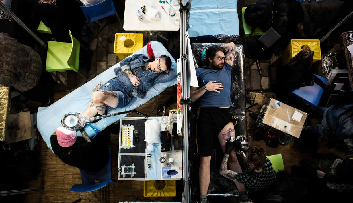 Seorang wanita dan pria bebaring ditato dalam acara Konvensi Tattoo Paris (Mondial du Tatouage) di Grand Halle de la Villette di Paris (8/3). Acara ini telah berlangsung dari tanggal 9-11 April 2018. (AFP/Philippe Lopez)
