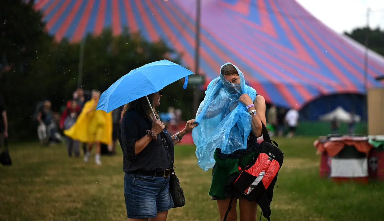 Pengunjung festival berlindung dari hujan pada hari pertama festival Glastonbury di desa Pilton, di Somerset, Inggris barat daya, pada 21 Juni 2023. (Photo by Oli SCARFF / AFP)