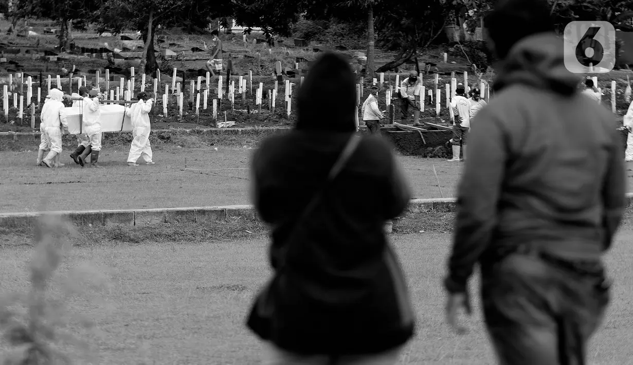Kerabat dan keluarga menyaksikan dari kejauhan proses pemakaman jenazah dengan protokol COVID-19 di TPU Bambu Apus, Jakarta, Kamis (28/1/2021). Hingga Kamis (28/1), di Indonesia, jumlah orang yang meninggal dunia akibat terpapar COVID-19 berjumlah 29.331 jiwa. (Liputan6.com/Helmi Fithriansyah)