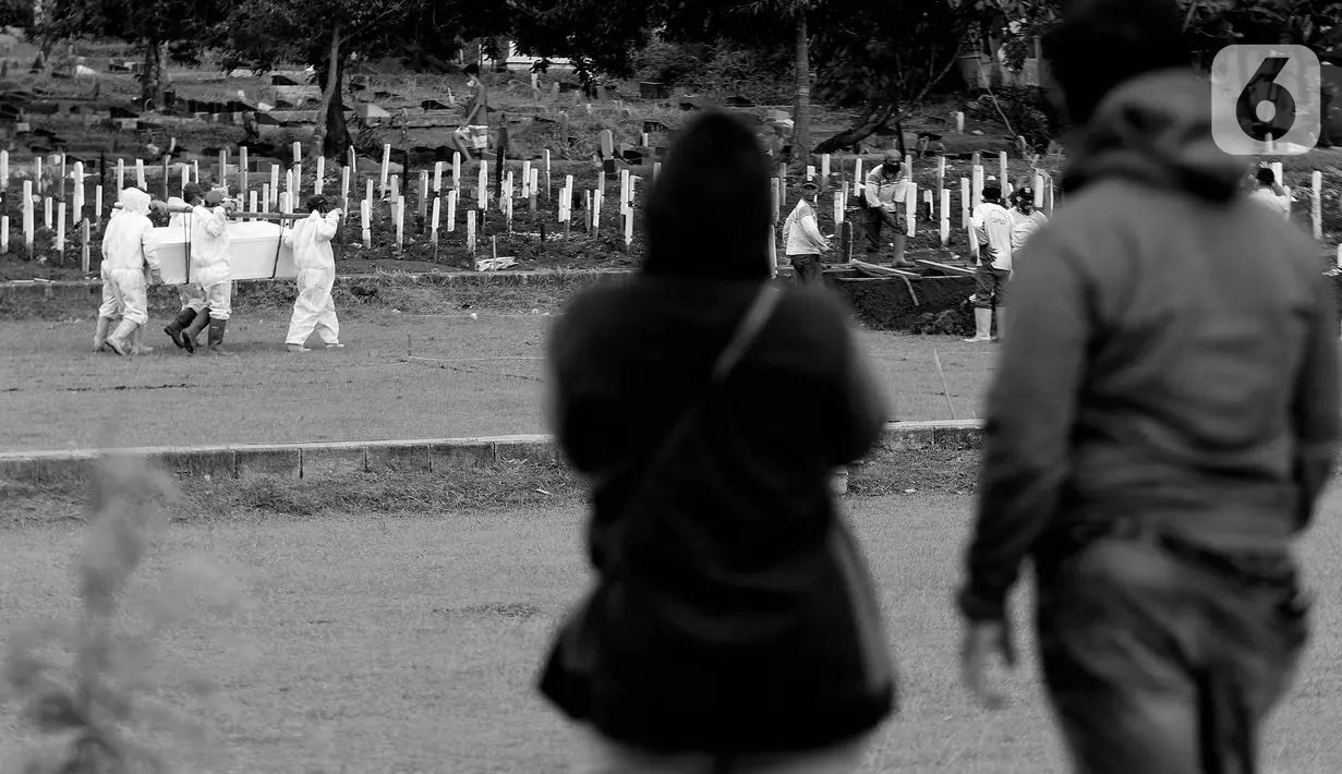 Kerabat dan keluarga menyaksikan dari kejauhan proses pemakaman jenazah dengan protokol COVID-19 di TPU Bambu Apus, Jakarta, Kamis (28/1/2021). Hingga Kamis (28/1), di Indonesia, jumlah orang yang meninggal dunia akibat terpapar COVID-19 berjumlah 29.331 jiwa. (Liputan6.com/Helmi Fithriansyah)