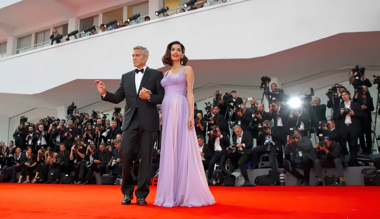 Pasangan selebritis, George dan Amal Clooney berpose untuk fotografer setibanya di Venice Film Festival ke-74, Italia, 2 September 2017. Di momen itu, Amal menebar pesonanya dalam balutan gaun sutra panjang koleksi Versace. (AP Photo/Domenico Stinellis)