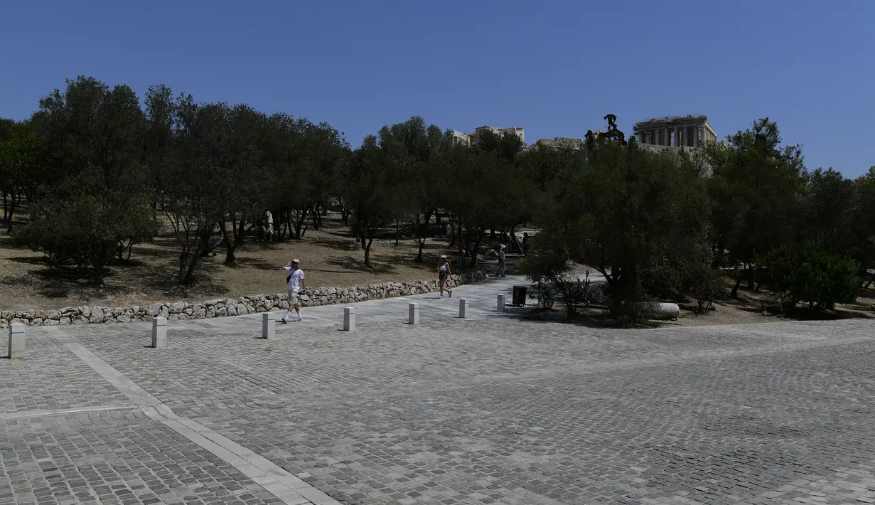 Orang-orang berjalan di bawah Acropolis kuno, di Athena Yunani, Selasa (3/8/2021). Pihak berwenang di Yunani telah menutup Acropolis dan situs kuno lainnya karena gelombang panas yang membakar Mediterania timur terus memburuk. (AP Photo/Michael Varaklas)