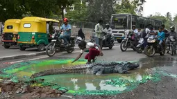 Sejumlah pengguna jalan memperhatikan aksi Seniman Baadal Nanjundaswamy saat menyelesaikan boneka buaya di atas jalan berlubang di Sultanpalya, Bangalore, India, Kamis (18/6/2015). (AFP PHOTO/ Manjunath KIRAN)