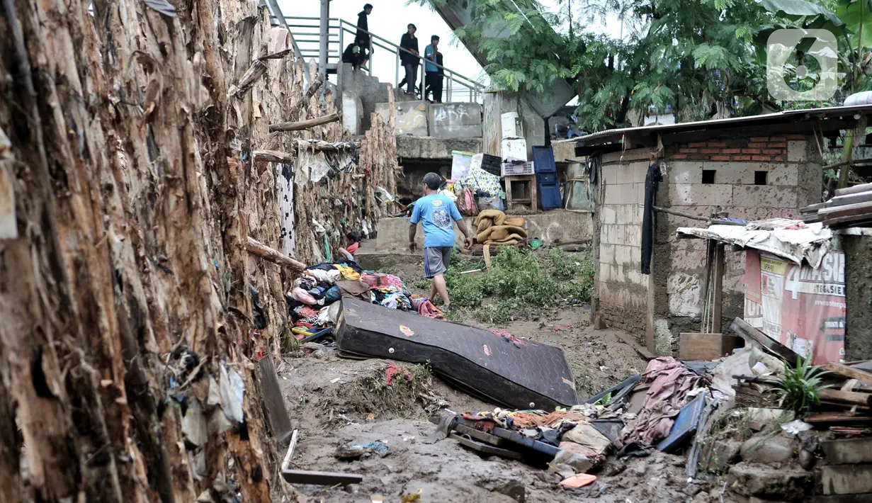 Warga berjalan di dekat tanggul batang pohon yang berada di bantaran Kali Ciliwung, Rawajati, Jakarta, Minggu (5/1/2020). Tanggul dari kayu dolken dan karung pasir yang baru dibangun pada akhir Desember 2019 itu rusak hingga dipenuhi sampah akibat terjangan arus banjir. (merdeka.com/Iqbal Nugroho)