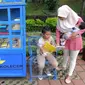 Seorang ibu menemani anaknya membaca buku yang tersedia di layanan Kotak Literasi Cerdas (Kolecer) di Taman Sempur, Bogor, Jawa Barat, Kamis (20/12). Kehadiran Kolecer bertujuan untuk menumbuhkan budaya literasi. (Merdeka.com/Arie Basuki)