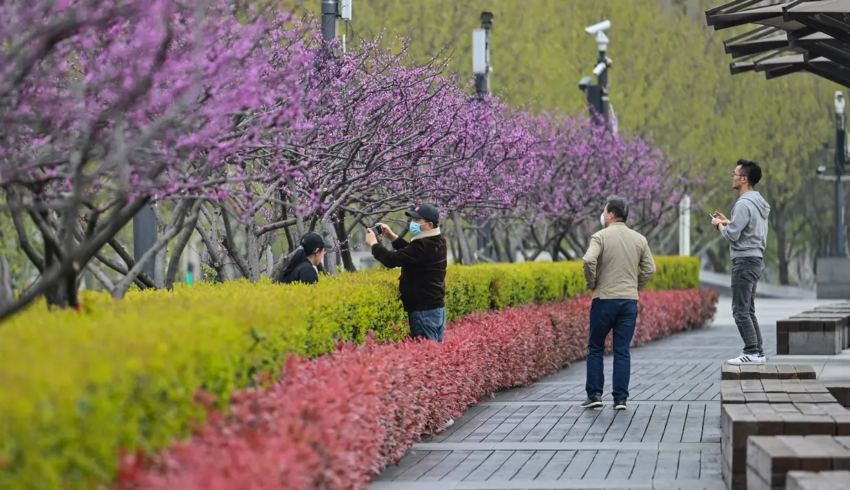 Orang-orang berjalan di sekitar Bund, sepanjang Sungai Huangpu, Puxi, Shanghai, 31 Maret 2022. Daerah Puxi akan lockdown mulai 1 April 2022. (Hector RETAMAL/AFP)