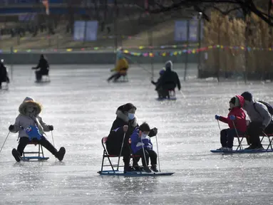 Seorang wanita dan anak-anak mendorong kursi es melintasi kolam beku di taman umum di Beijing, Selasa (17/1/2023). China telah mengumumkan penurunan populasi pertamanya dalam beberapa dasawarsa seiring bertambahnya usia negara terpadat di dunia dan angka kelahirannya yang menurun. (AP Photo/Mark Schiefelbein)